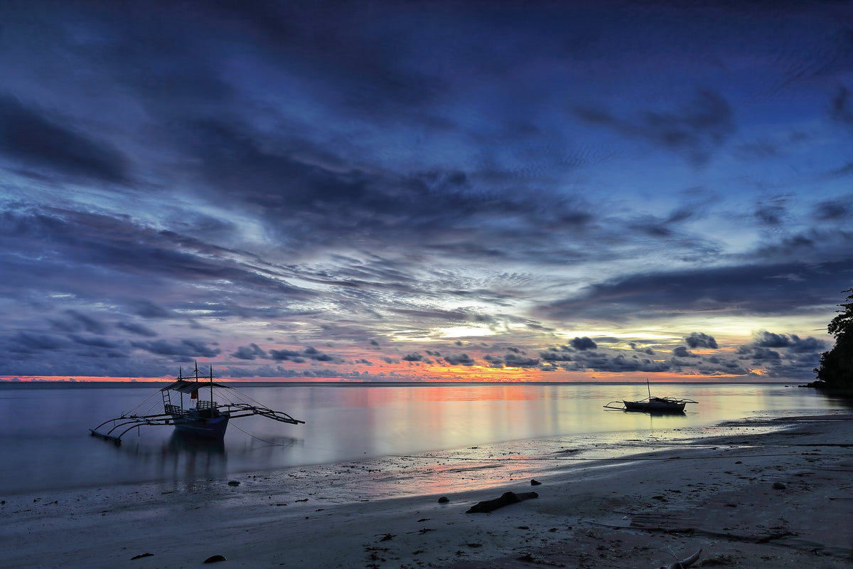 Outrigger boats on Punta Ballo beach at dusk in Sipalay, Philippines