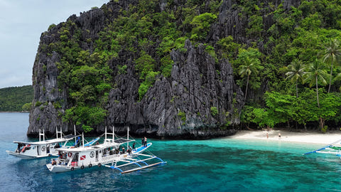 Palawan Divers boat beside a limestone island and white-sand beach in Bacuit Bay
