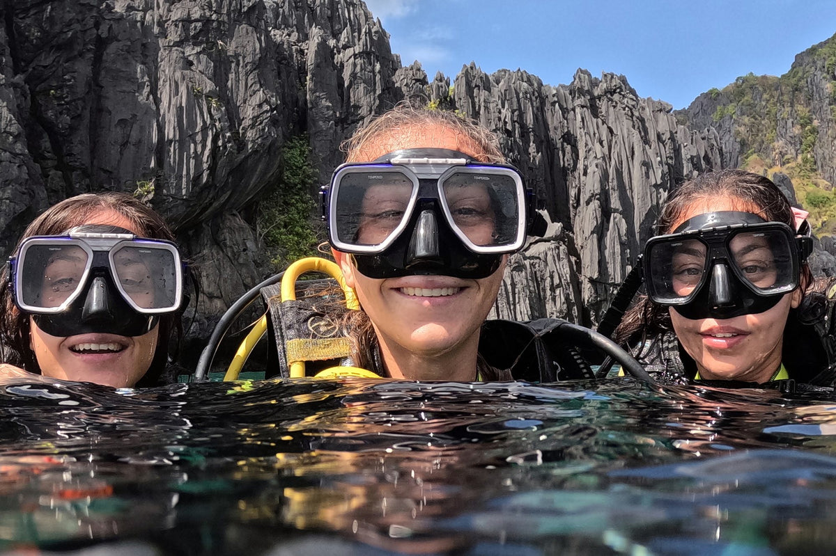 Three divers at the surface below limestone cliffs in El Nido